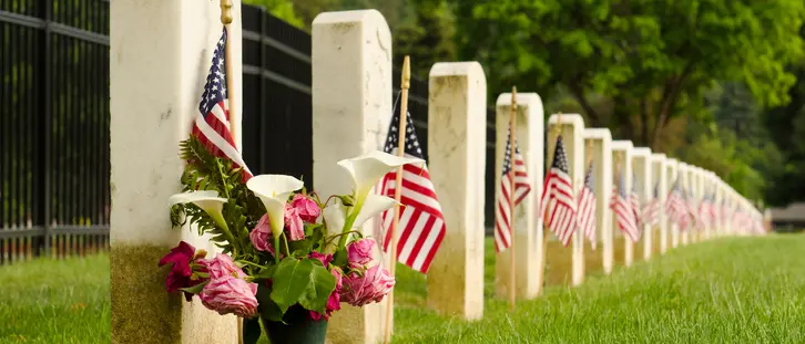 American flags and flowers placed by rows of white gravestones in a cemetery