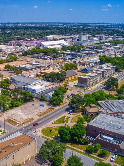 Aerial view of a suburban town with roads, buildings, trees, and distant coastline under a blue sky