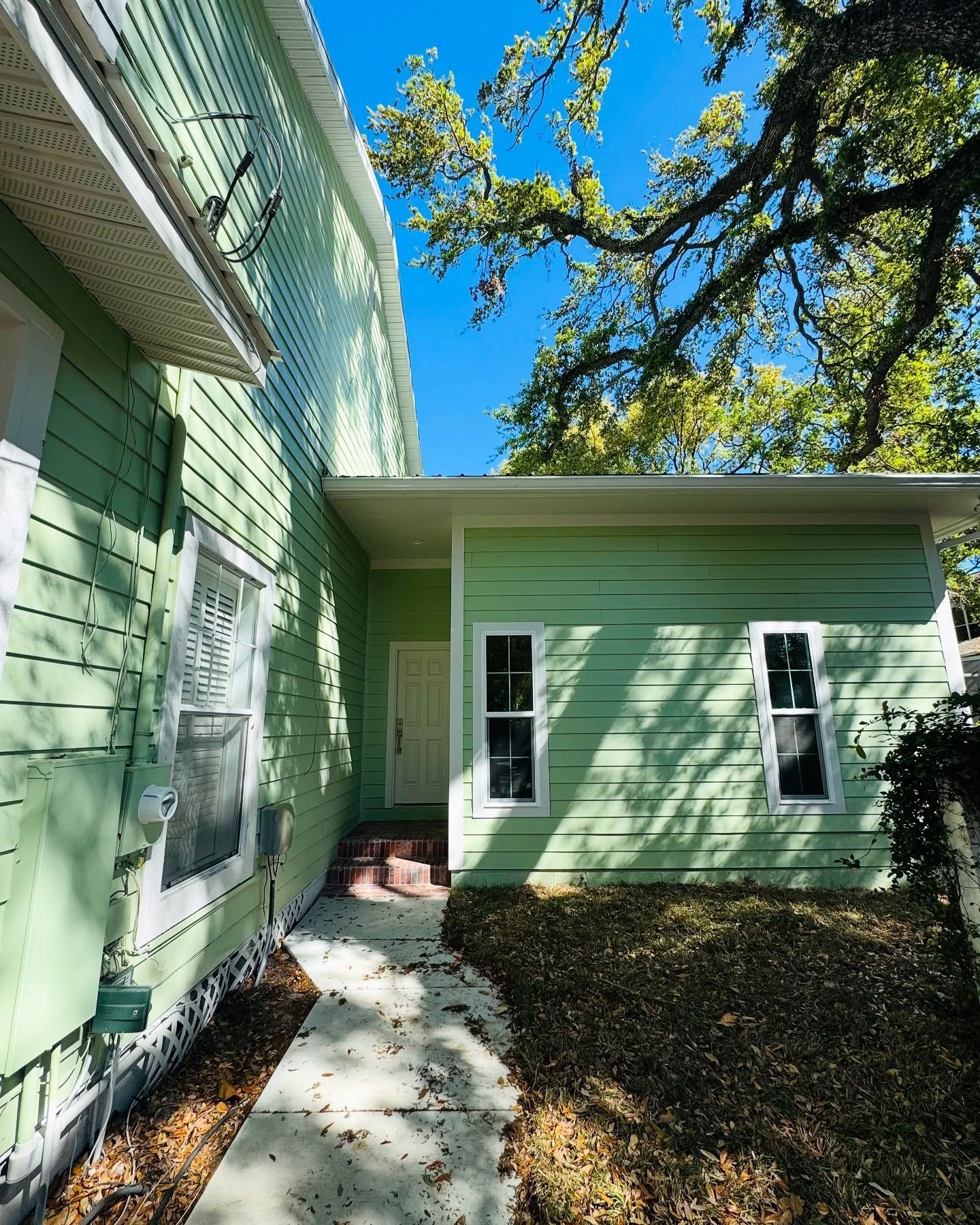 Light green house with white trim, side view, pathway to front door, blue sky, trees.