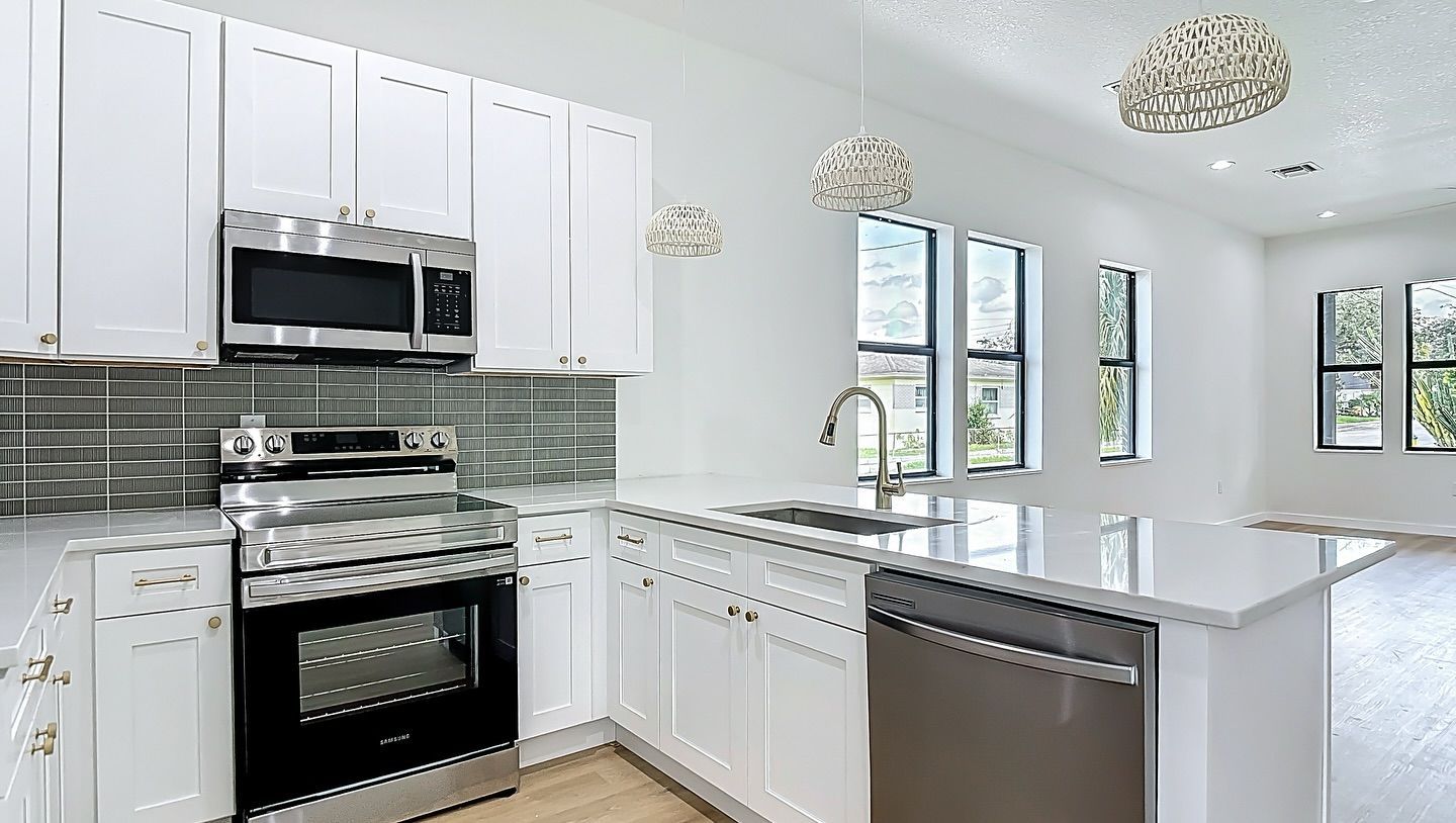 White kitchen with stainless steel appliances, white cabinets, and large windows.