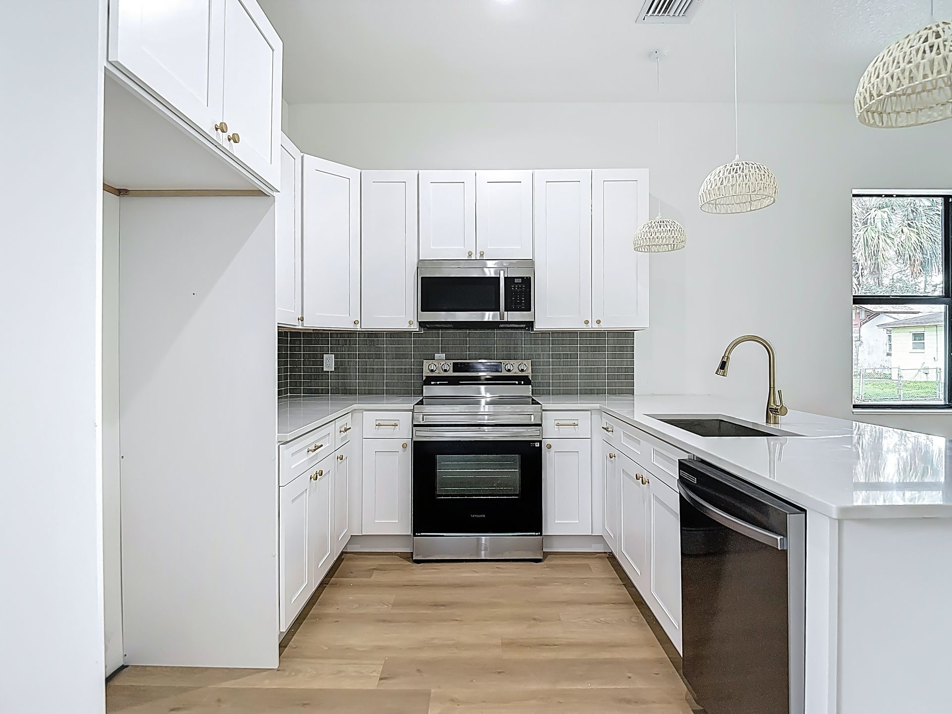 White kitchen with cabinets, appliances, light countertops, backsplash, and wood-look flooring.