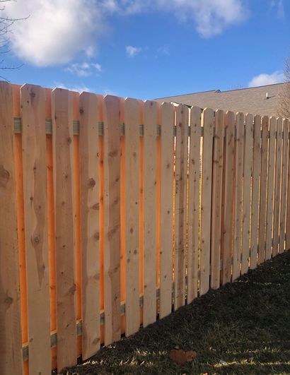 Wooden backyard fence with fresh vertical slats under a blue sky.
