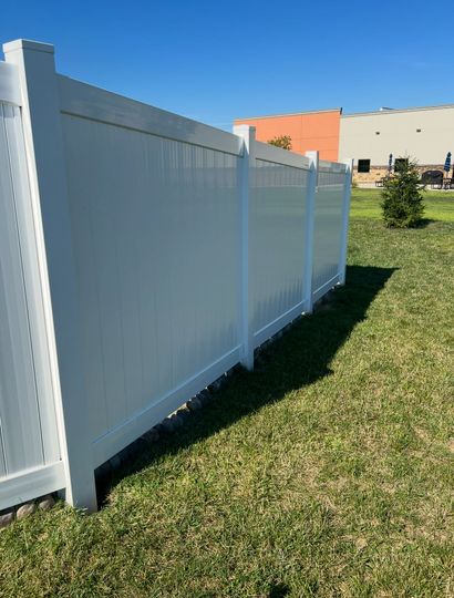 White vinyl fence in a grassy yard beside a building on a sunny day