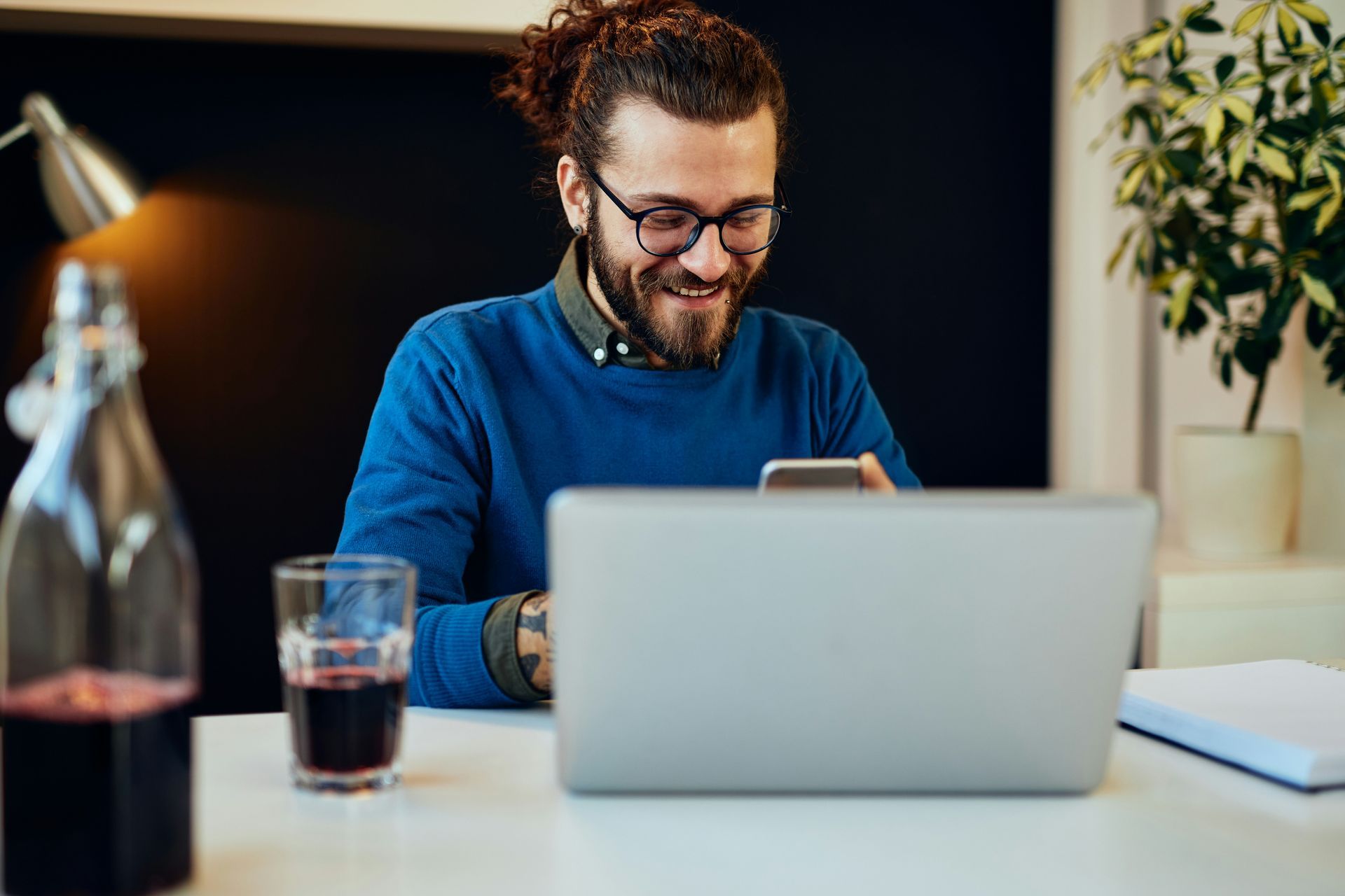 A man is sitting at a desk using a laptop computer and a cell phone.