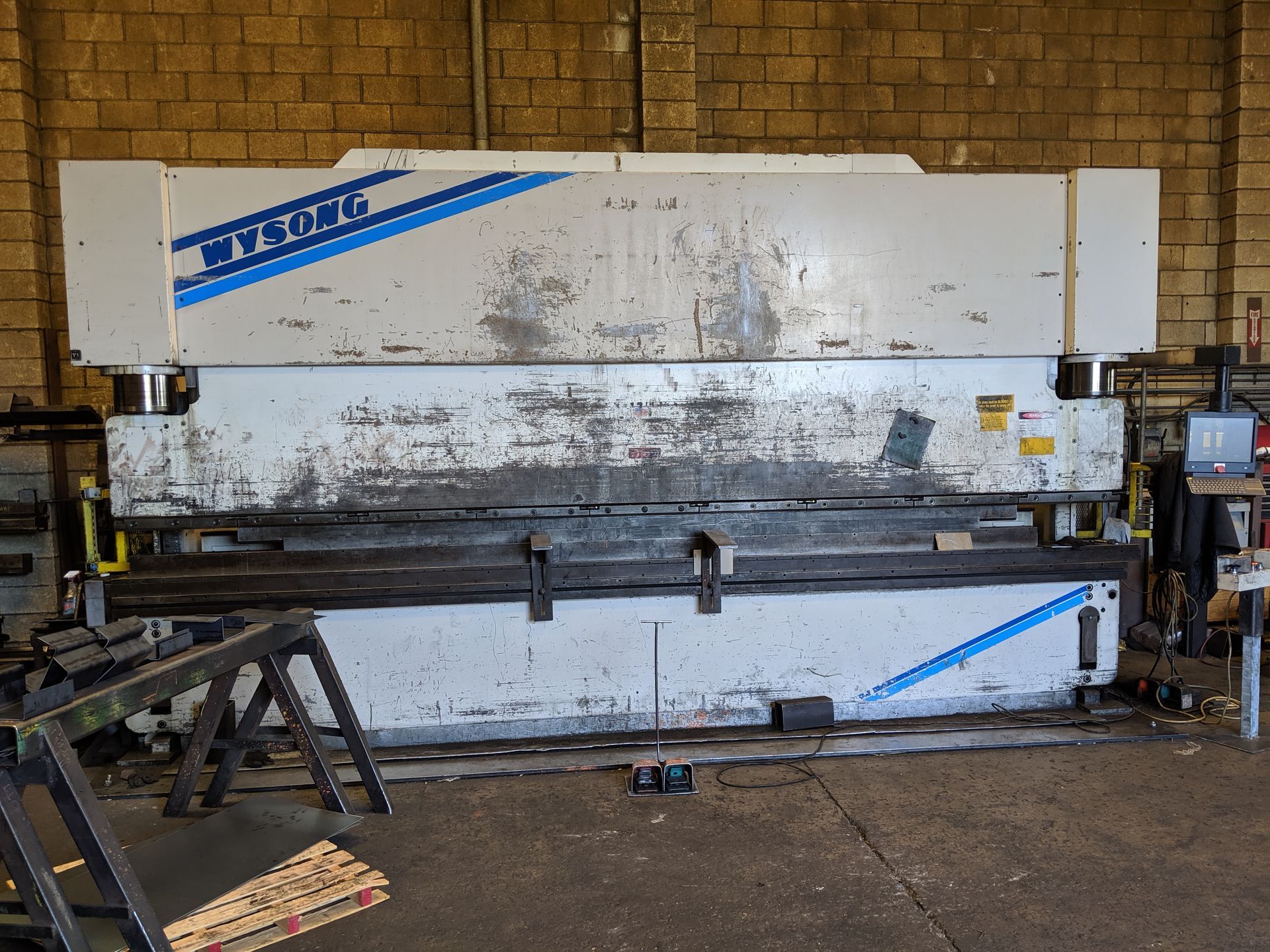 Large industrial metal sheet brake machine in a workshop with worn white panels and blue accents
