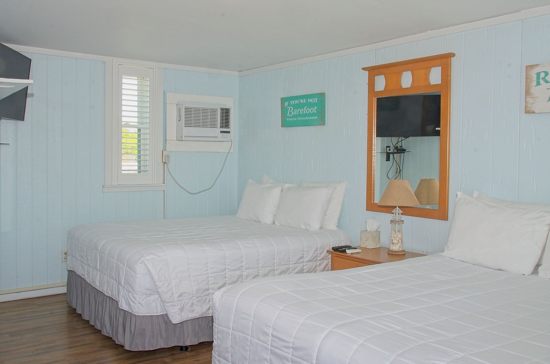 A motel room with two queen beds, light blue paneling, a window, and a mounted TV.