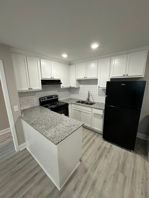 A kitchen with white cabinets , a black refrigerator , a stove , and a sink.