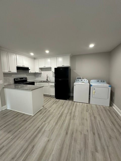 A kitchen with a refrigerator , washer and dryer , and wooden floors.