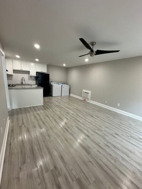 A living room with a ceiling fan and a kitchen in the background.
