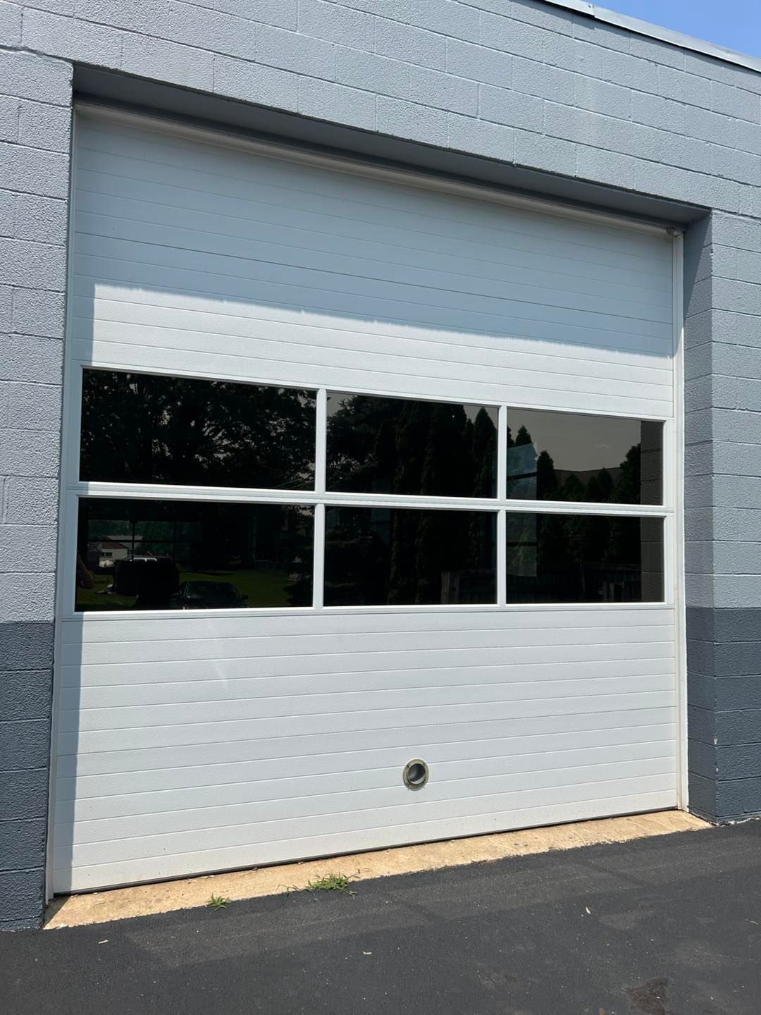 A white sectional garage door with a row of three glass windows, set into a grey cinder block wall.