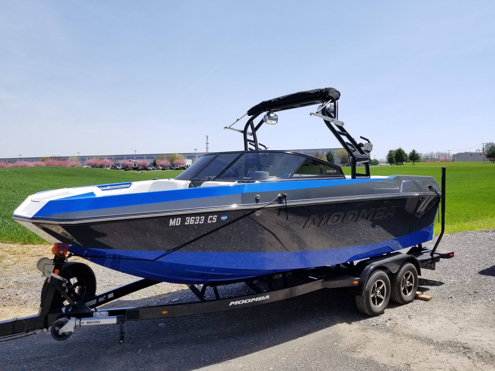 A teal and white wakeboard boat on a trailer parked in a residential driveway.