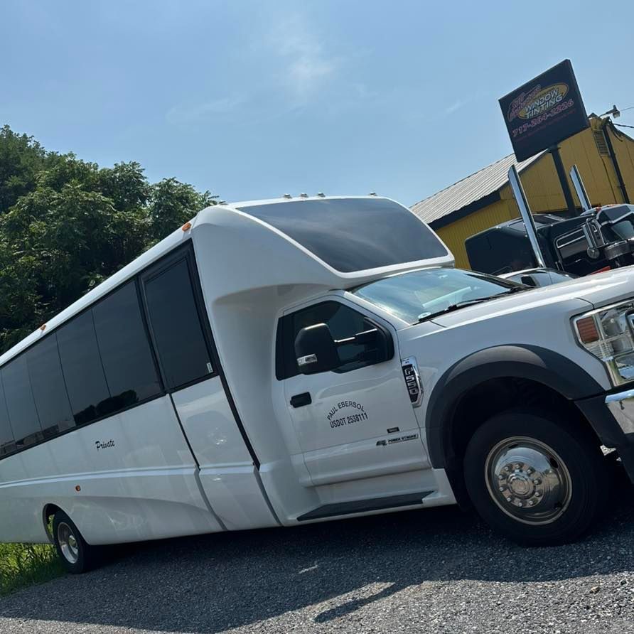 A white Ford shuttle bus parked on a gravel lot under a bright blue sky.
