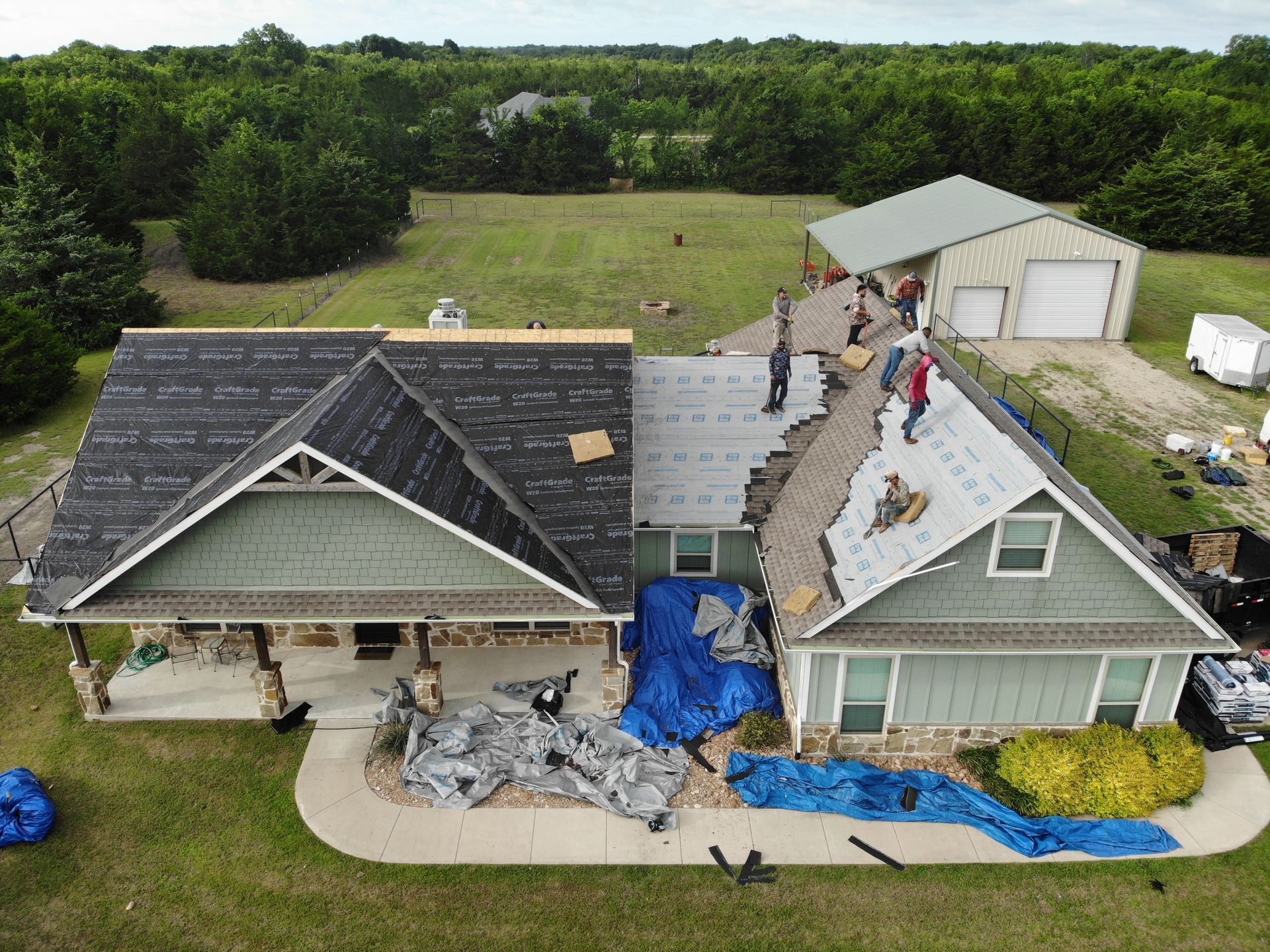Storm-damaged house with roof torn open, debris on lawn, and people inspecting damage from above.