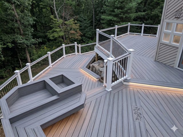 A multi-level gray composite deck features built-in bench seating, white railings, integrated lighting, and a tree cutout.