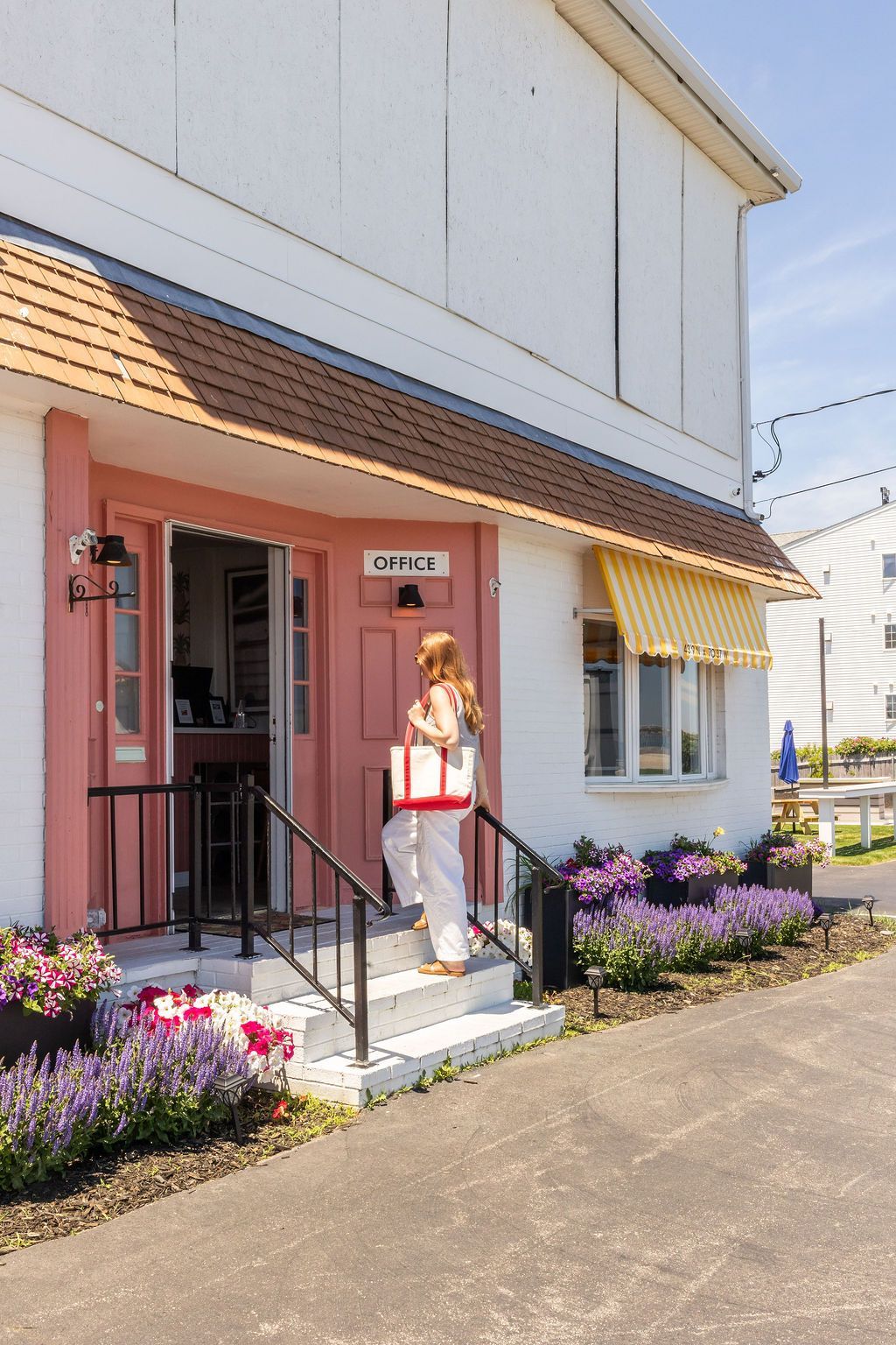 A white two-story building with yellow striped awnings, a red front door, and two lounge chairs in front.