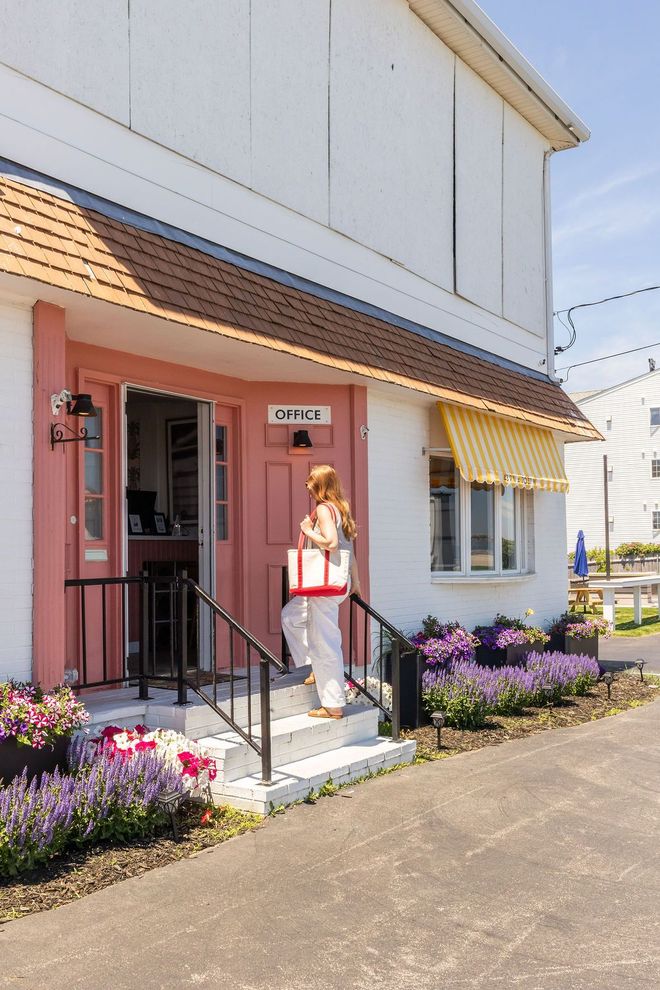 A white two-story building with yellow striped awnings, a red front door, and two lounge chairs in front.