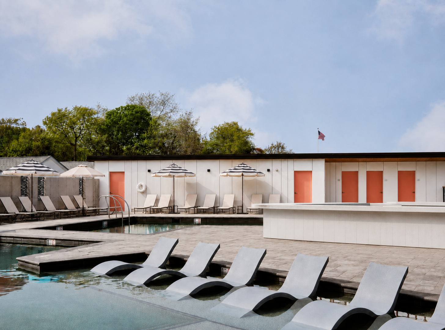A rectangular swimming pool with lounge chairs sitting in the shallow end, surrounded by a deck and small cabanas.