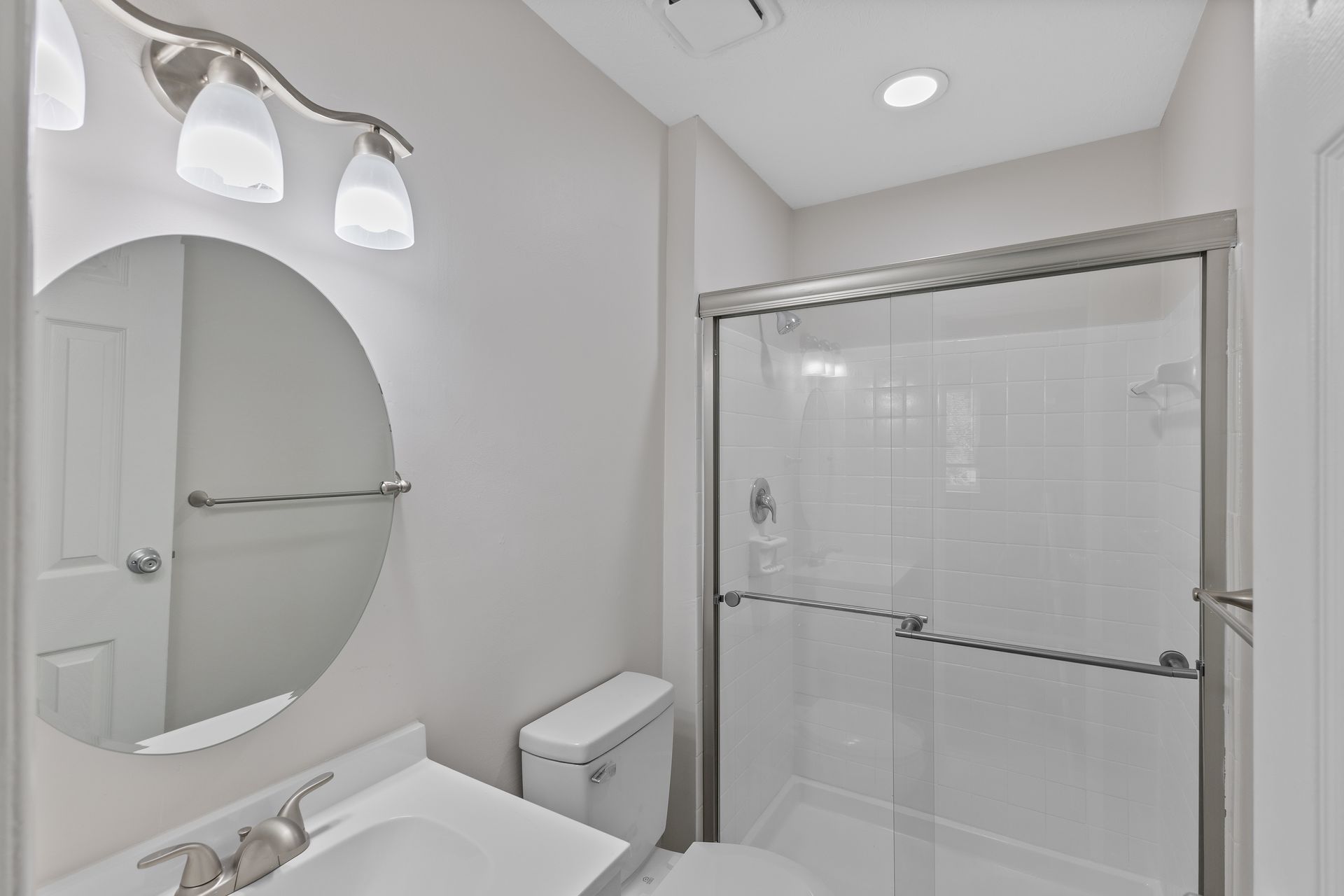 Renovated bathroom with glass shower, round mirror, vanity lighting, and modern fixtures.