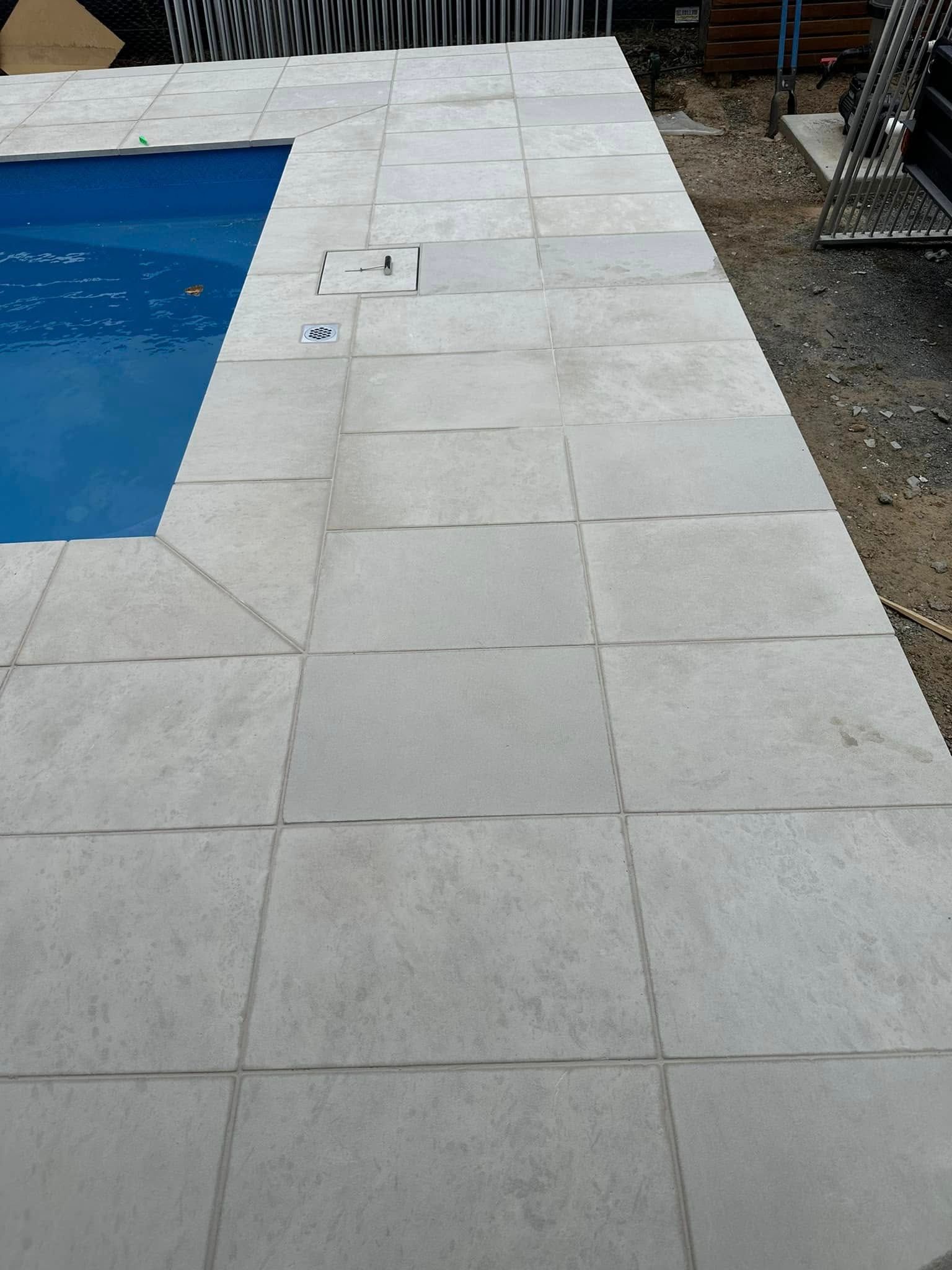 Poolside area with light gray square paving tiles. The blue water is on the left. — East Coast Paving in Seaham, NSW