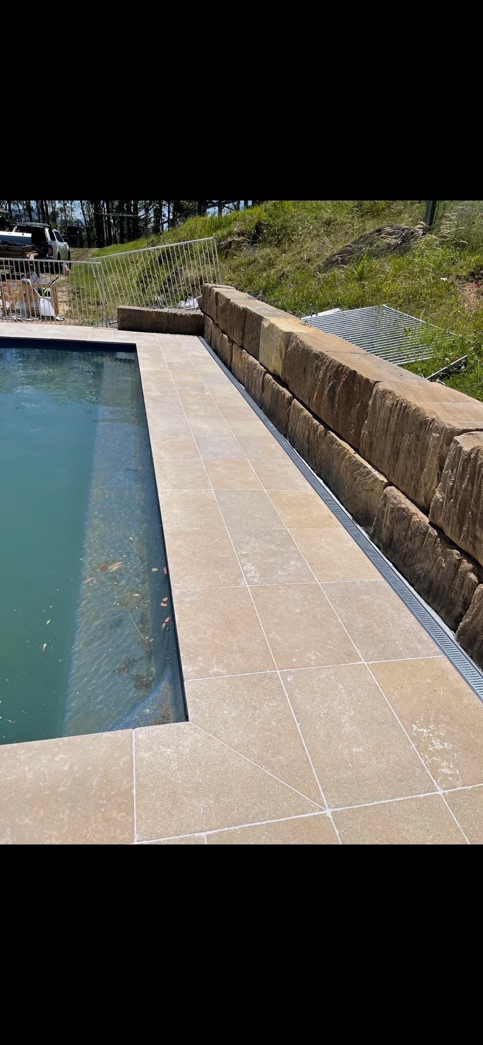 A Pool With a Concrete Border, a Stone Retaining Wall, and Green Grass — East Coast Paving in Raymond Terrace, NSW