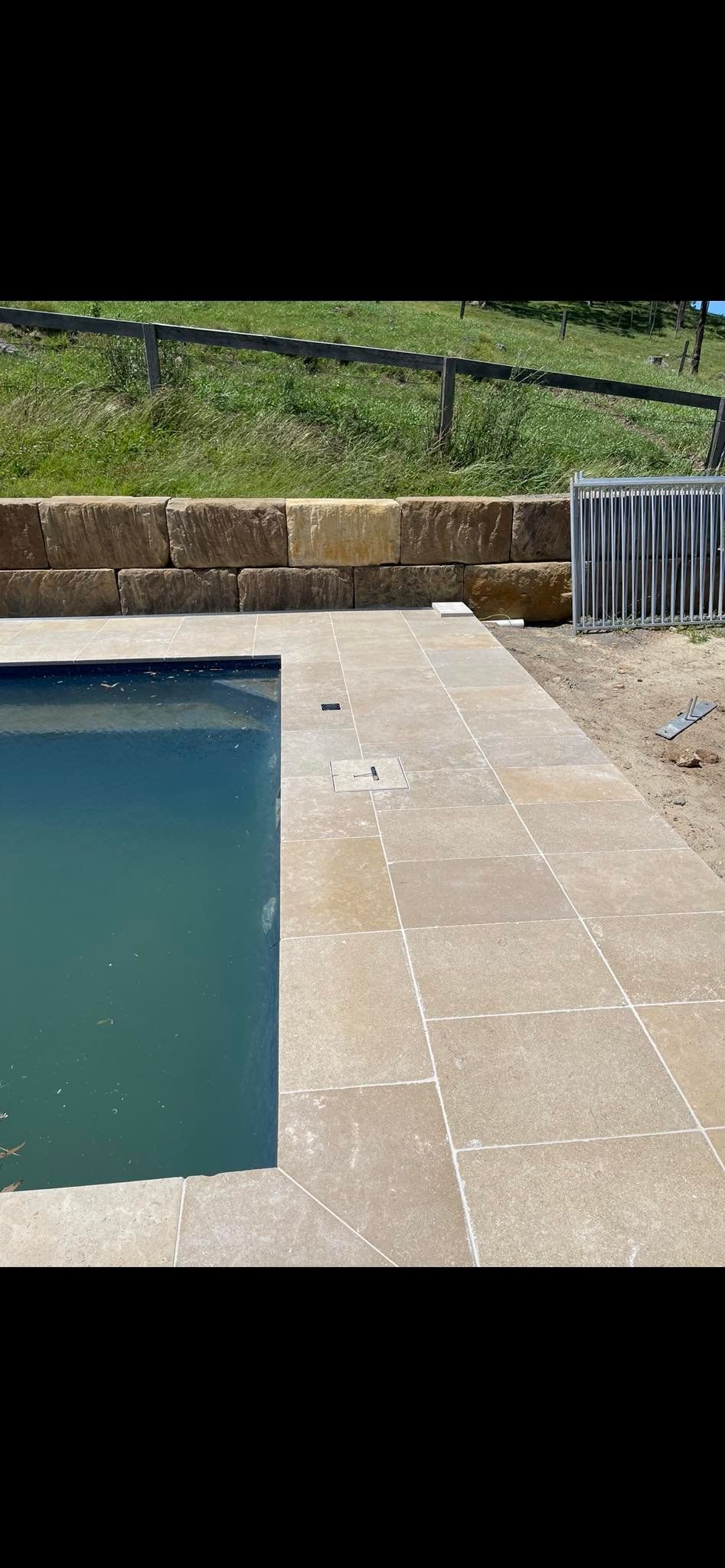 A swimming pool with tan stone paving and a retaining wall — East Coast Paving in Seaham, NSW