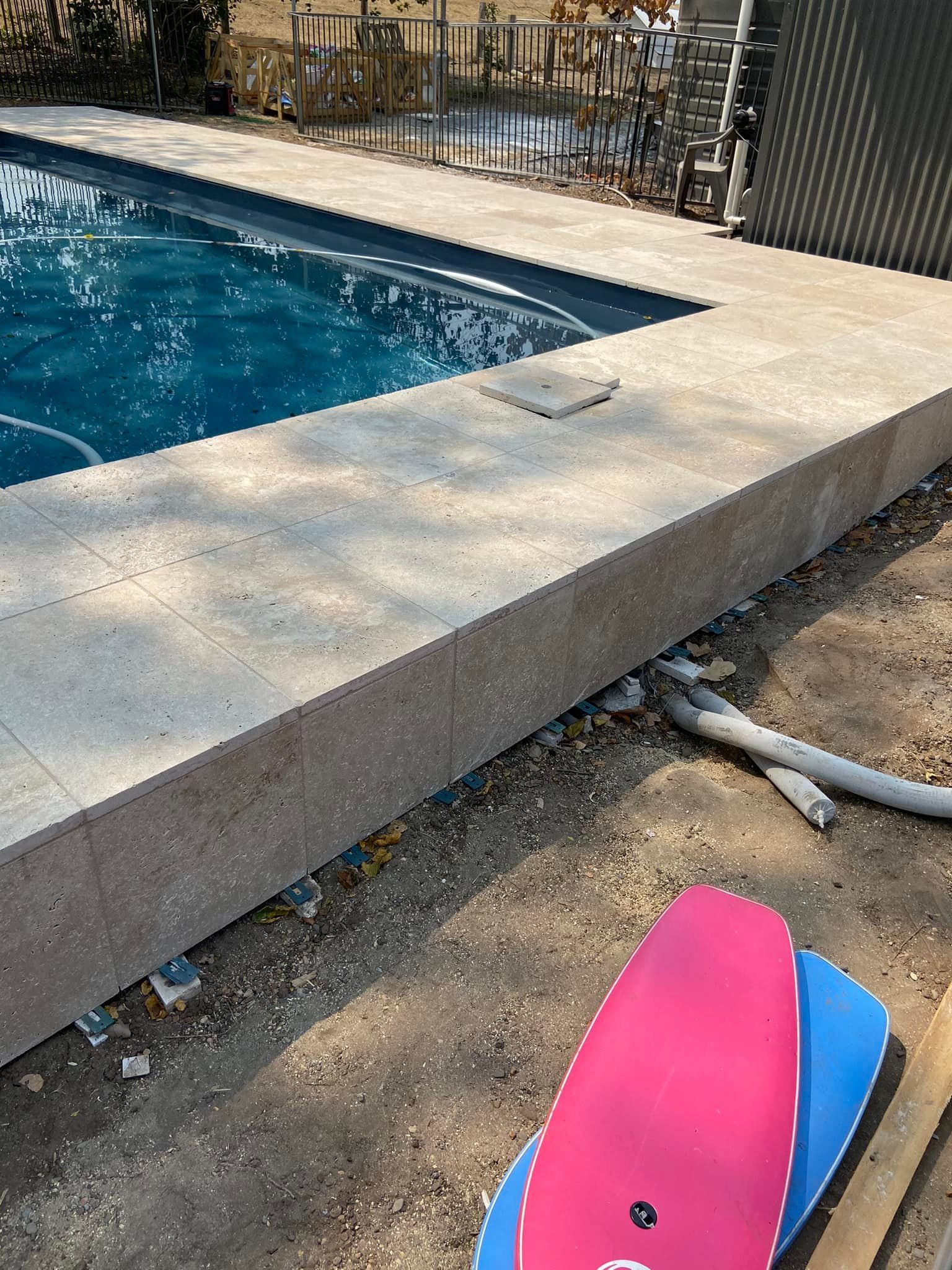 Pool with concrete coping and pink and blue surfboards on the ground. — East Coast Paving in Seaham, NSW