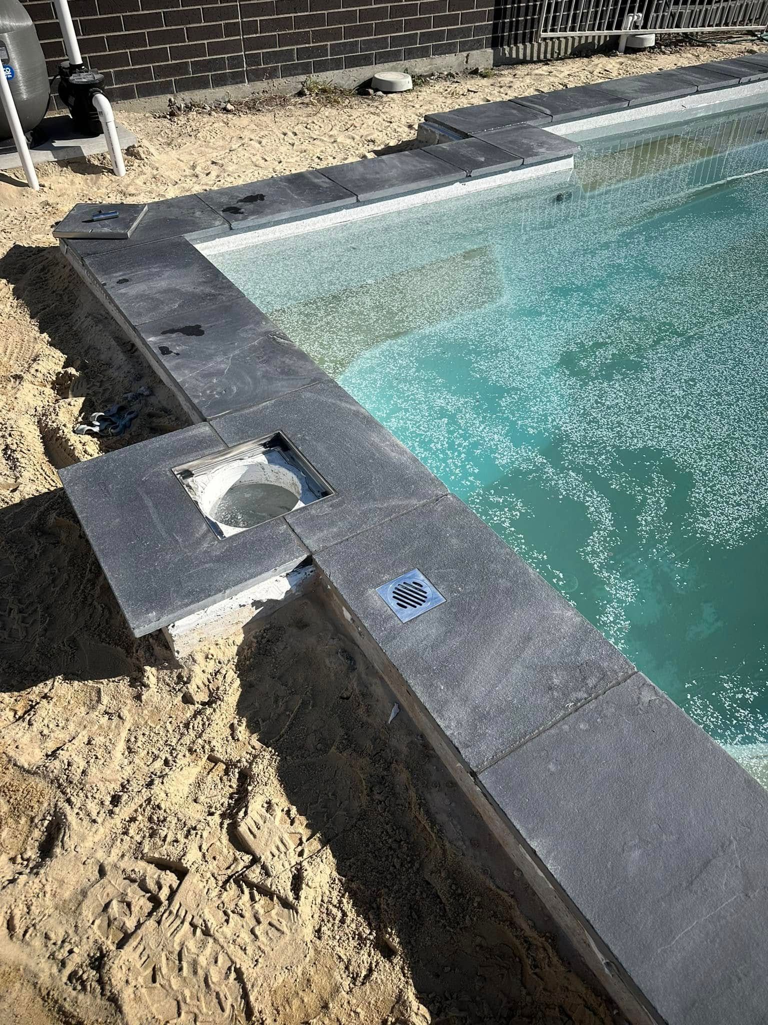 Pool under construction; dark gray border with water; sand in foreground — East Coast Paving in Seaham, NSW