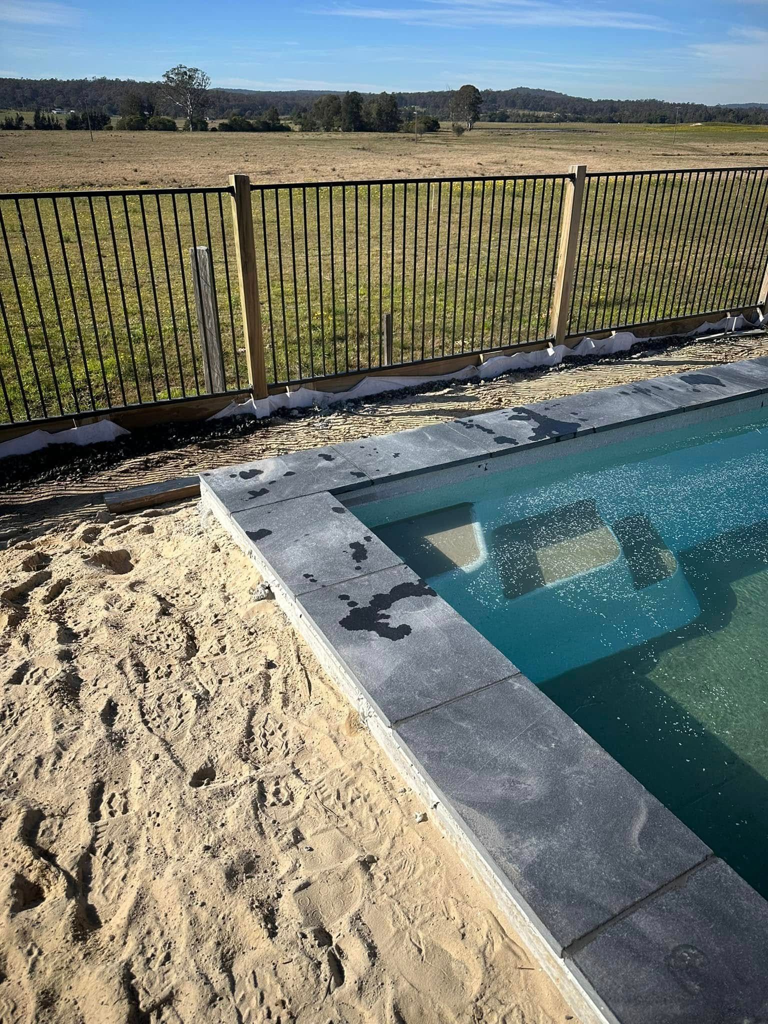 Pool With Stone Coping, Sand, and Woven Black Fence in a Rural Setting — East Coast Paving in Raymond Terrace, NSW