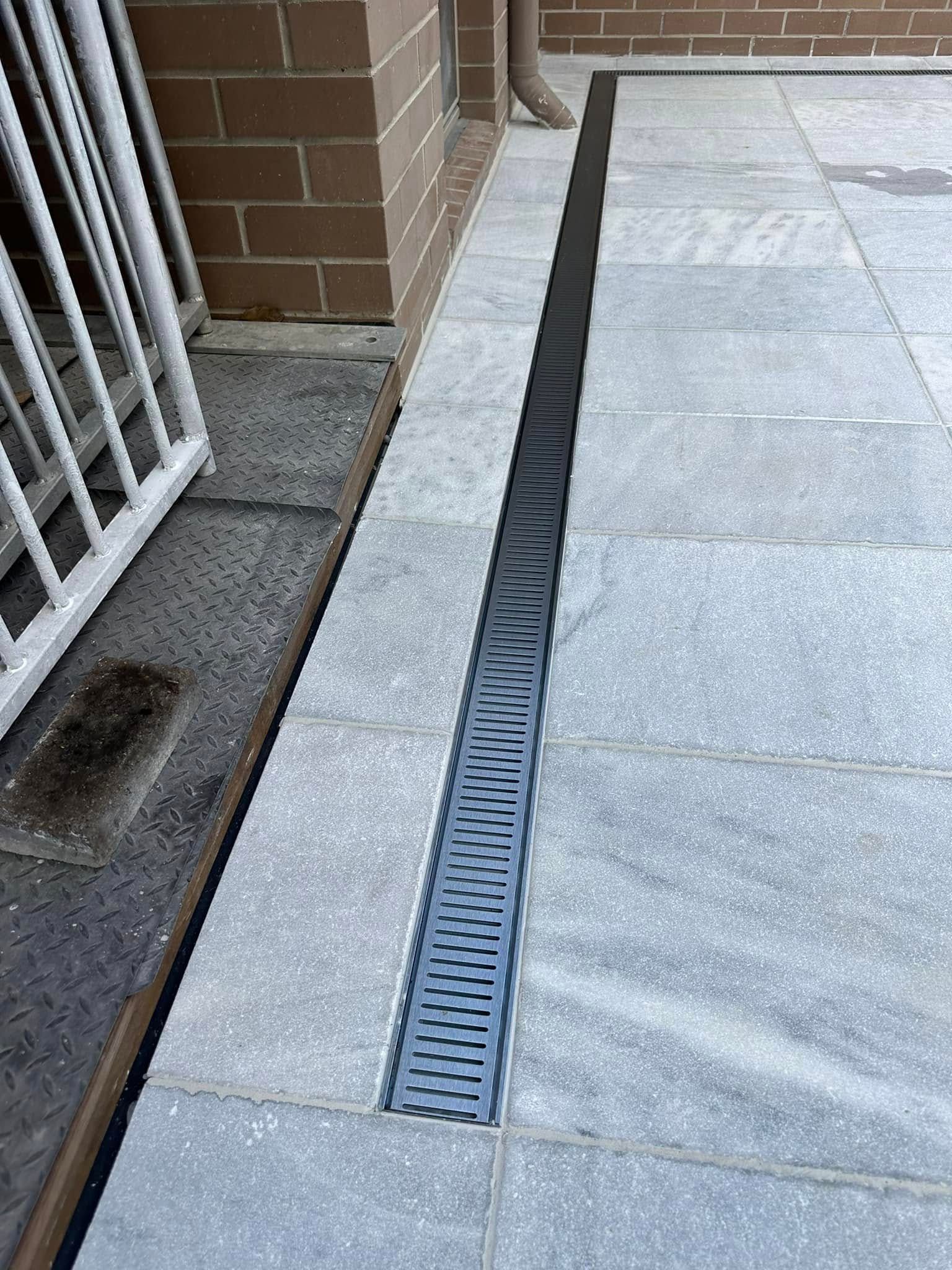 Gray Tiled Patio With a Linear Drain Next to a Brick Wall — East Coast Paving in Medowie, NSW