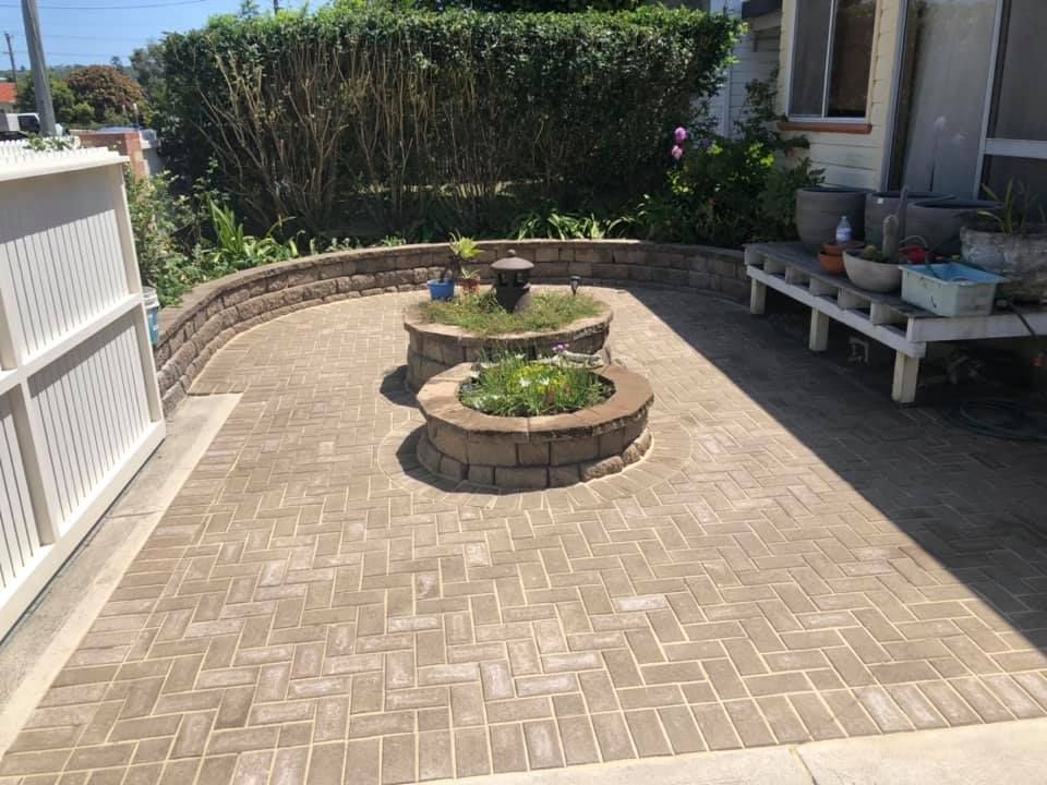 Brick Patio With Two Tiered Planters, a White Fence, and Greenery in a Sunny Setting — East Coast Paving in Medowie, NSW