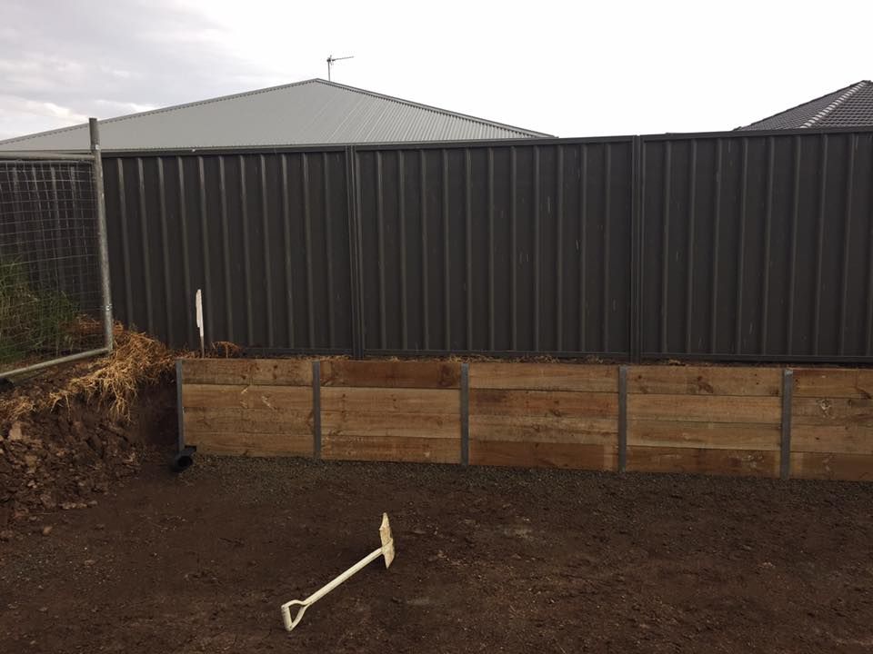 A wooden retaining wall in a yard, against a dark grey corrugated fence — East Coast Paving in Seaham, NSW