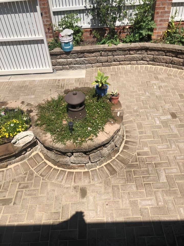 Brick Patio With Circular Brick Planter, Surrounding Stonewall, and White Fence — East Coast Paving in Raymond Terrace, NSW
