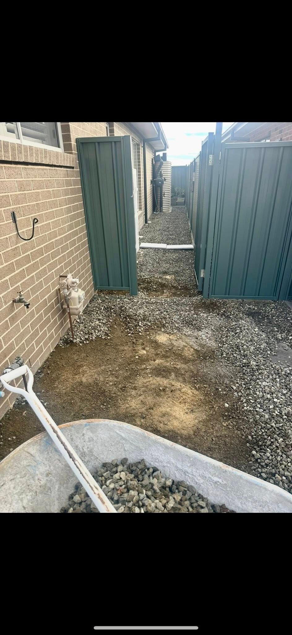 Narrow outdoor walkway with gravel, between a brick wall and green panels — East Coast Paving in Seaham, NSW