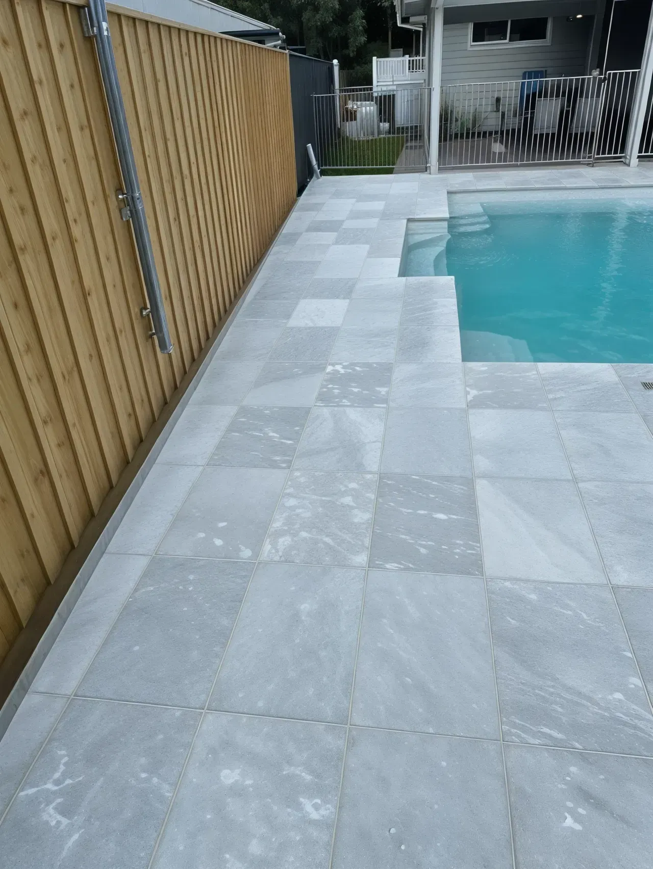 Poolside With Light Gray Tiled Paving Next to a Wooden Fence and Pool — East Coast Paving in Medowie, NSW