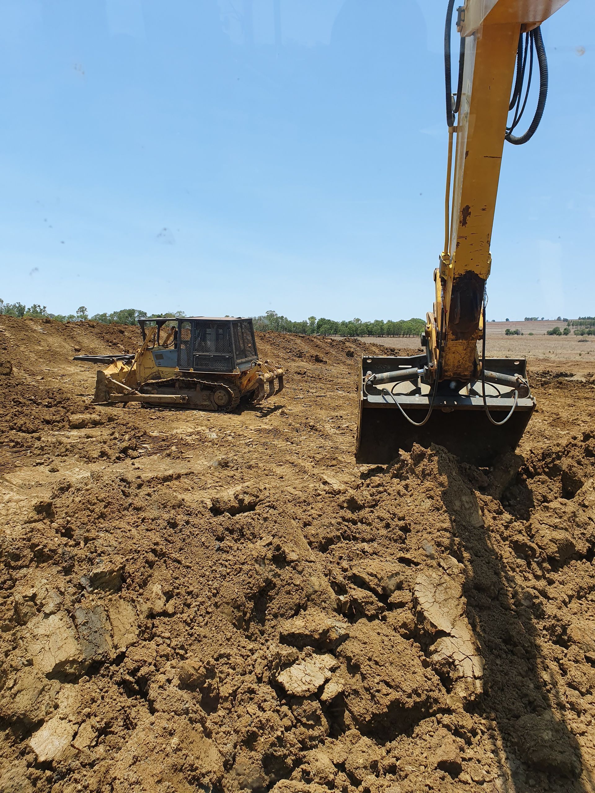 A Bulldozer Is Digging A Hole In The Dirt Next To An Excavator — Greenslade's Dozer & Excavator Hire Pty Ltd In Manumbar, QLD