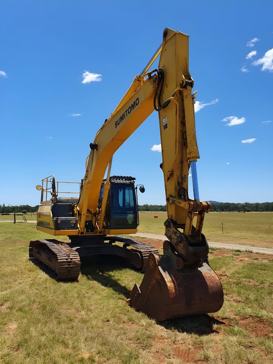 A Yellow Excavator Is Parked In A Grassy Field — Greenslade's Dozer & Excavator Hire Pty Ltd In Manumbar, QLD