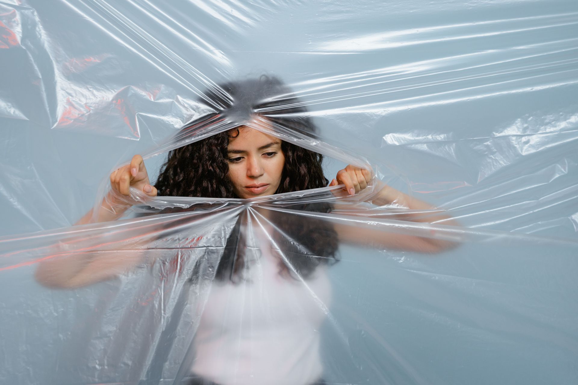 Woman pulling apart clear plastic sheeting in a pale blue studio scene
