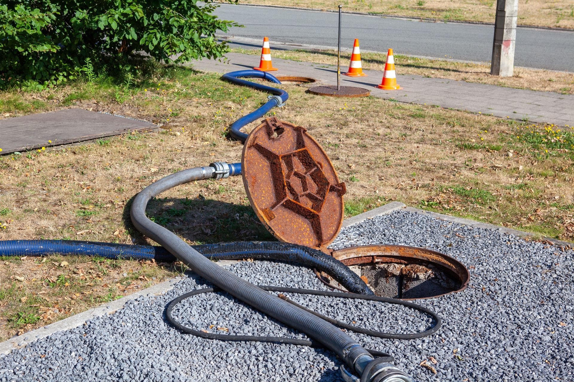 A manhole cover is open and a hose is connected to it.