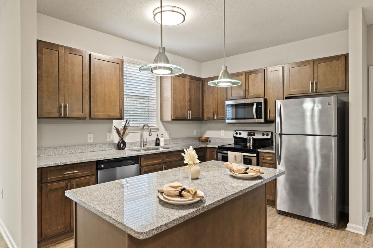 Interior kitchen with an island, granite countertops, wood cabinets, and stainless steel appliances.