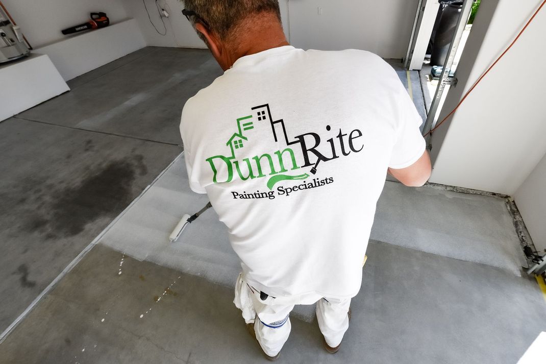 A man wearing a dunn rite shirt is painting a floor