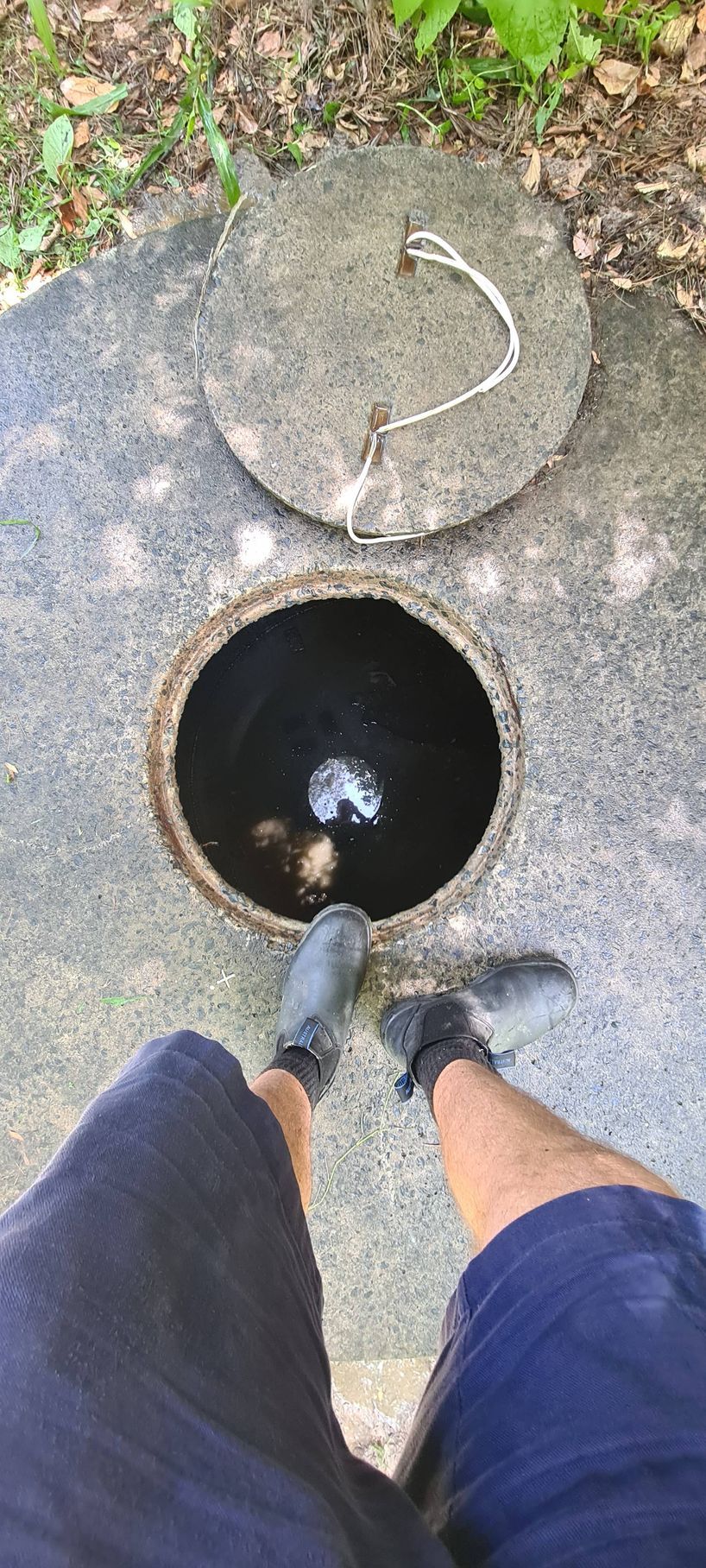 Person standing over an open sewer access. The cover is partially open — Raptor Waste Management in Coolangatta, QLD
