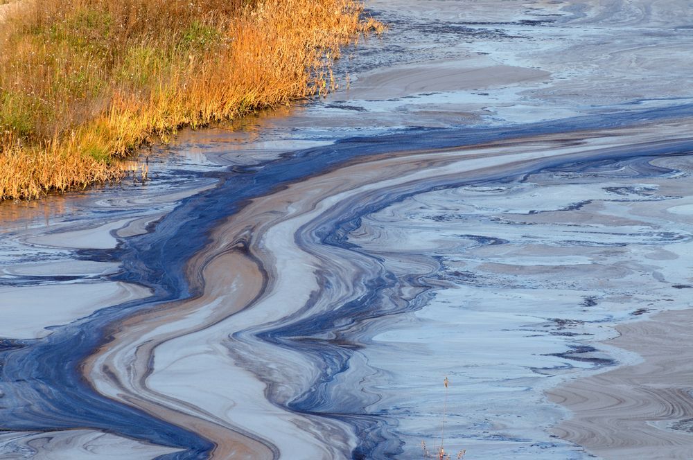 Polluted Water With Dark Blue Streaks Flowing Through a Tan — Raptor Waste Management In Tweed Heads, NSW