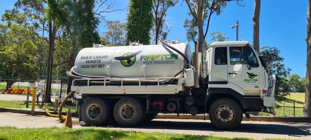 White septic tank truck parked on a paved road, connected to a hose. Trees in the background. — Raptor Waste Management in Coolangatta, QLD