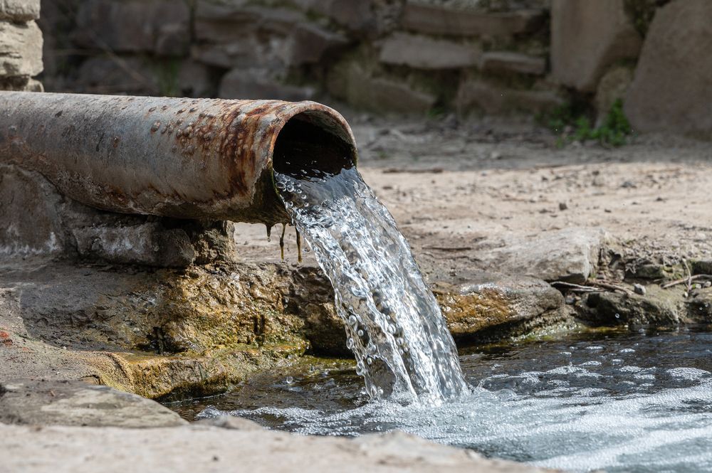 Rusty Pipe Pouring Clear Water Into a Stone-lined Pool — Raptor Waste Management In Pottsville, NSW