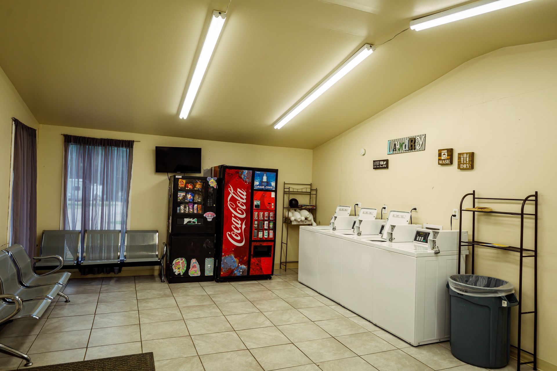 Empty break room with vending machines, counter, sink, and folding chairs on a tiled floor.