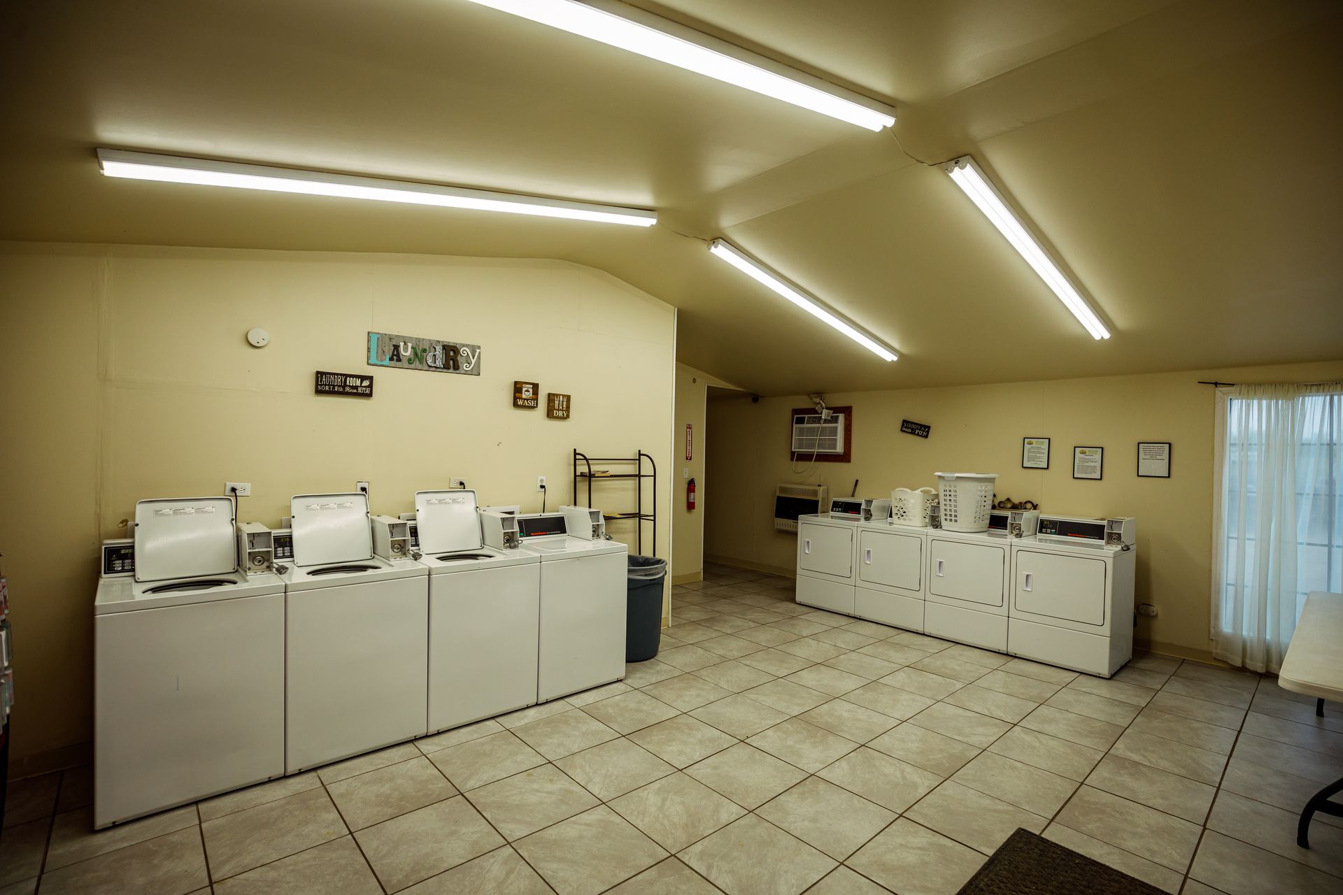 Laundry room with rows of white washers and dryers under bright fluorescent lights