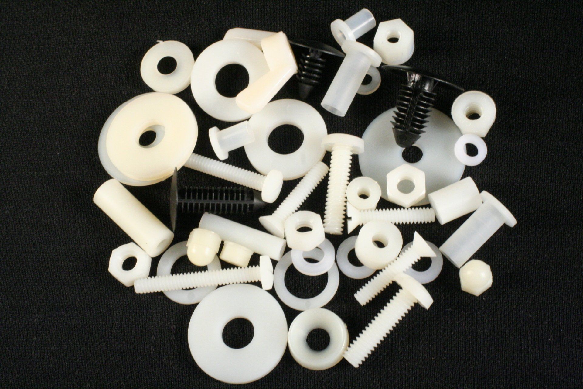 A pile of white plastic nuts and bolts on a black surface