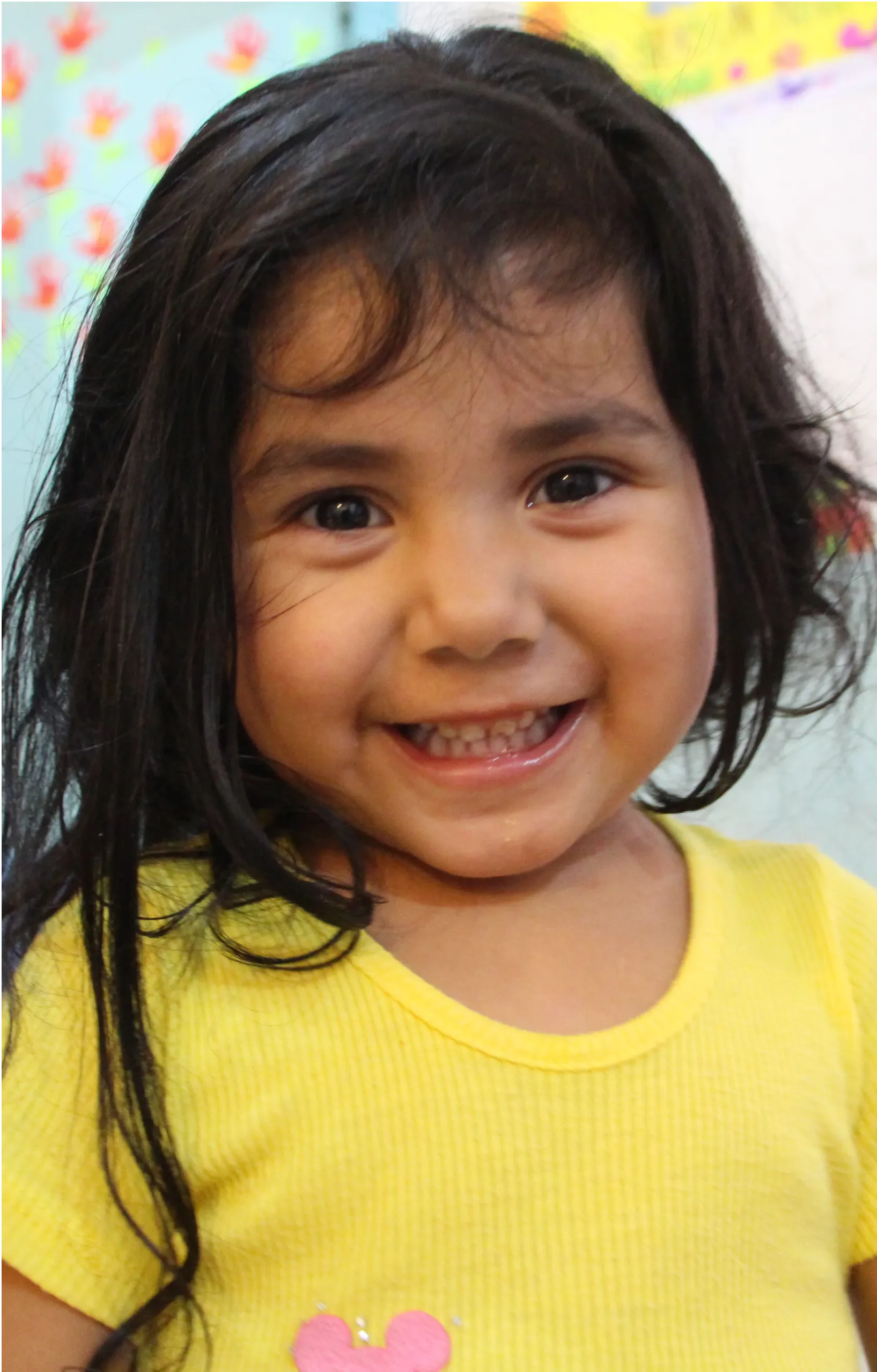 A little girl in a yellow shirt is smiling for the camera