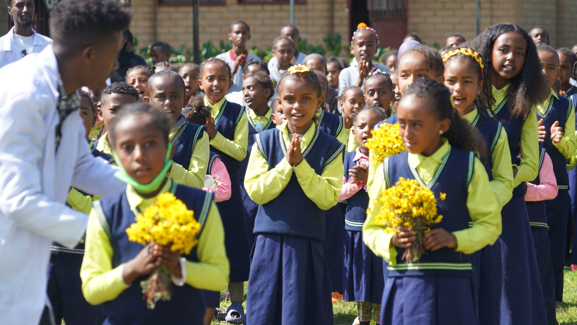 A group of children in school uniforms are holding bouquets of yellow flowers.