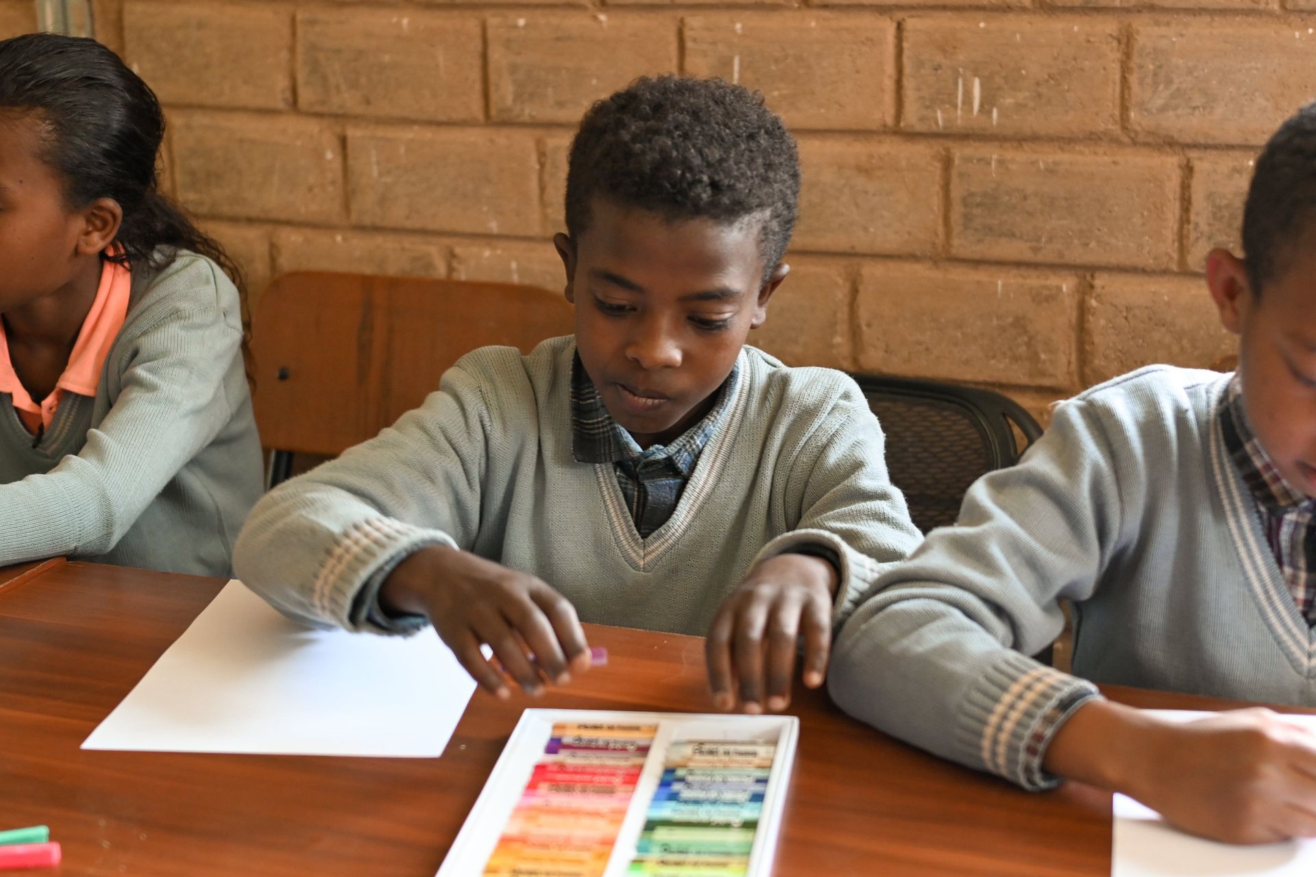 A group of children are sitting at a table with crayons
